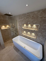 Completed bathroom with freestanding bath and lit stone-tiled alcoves