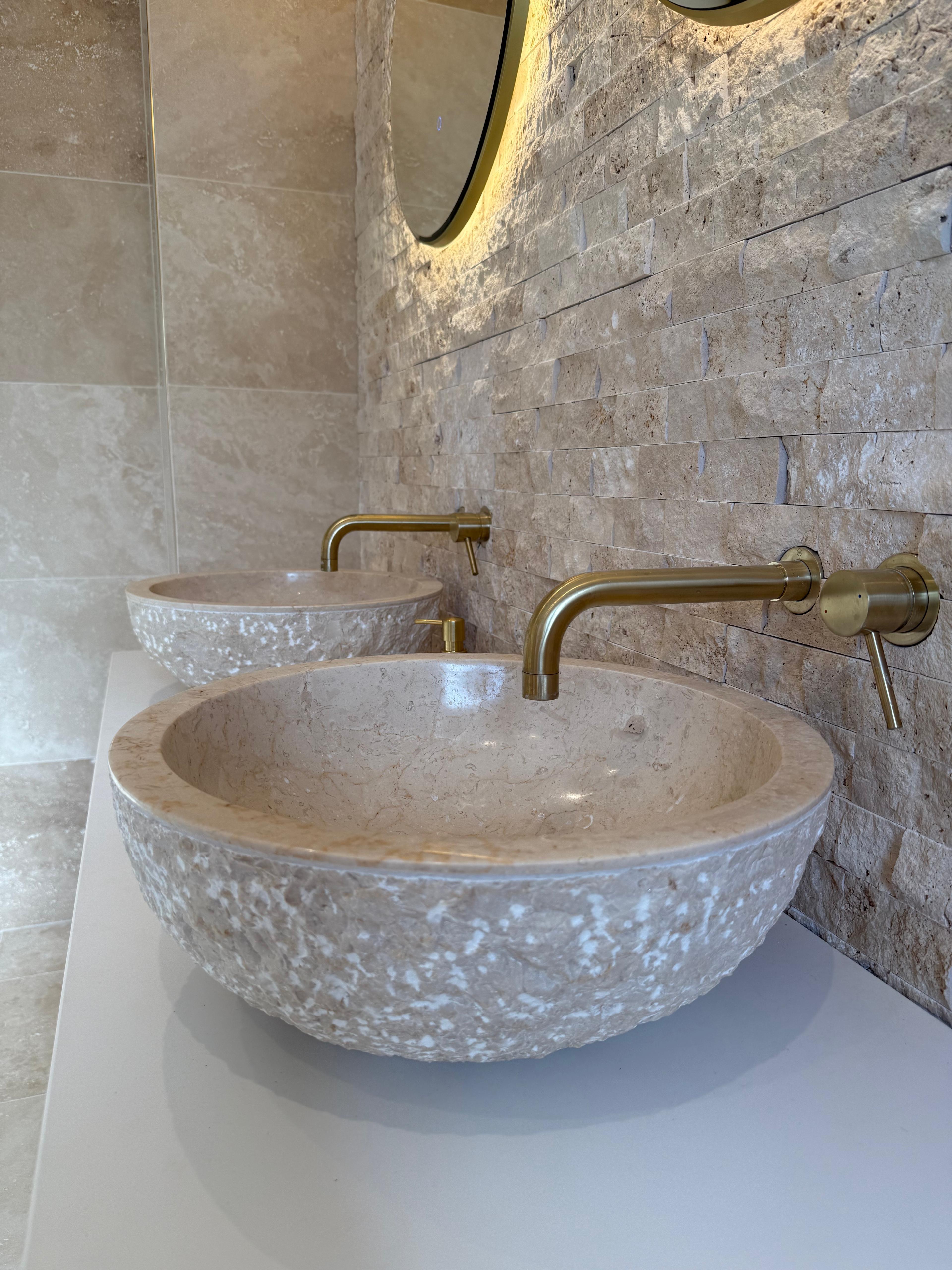 Stone vessel basin with a brushed brass wall-mounted tap