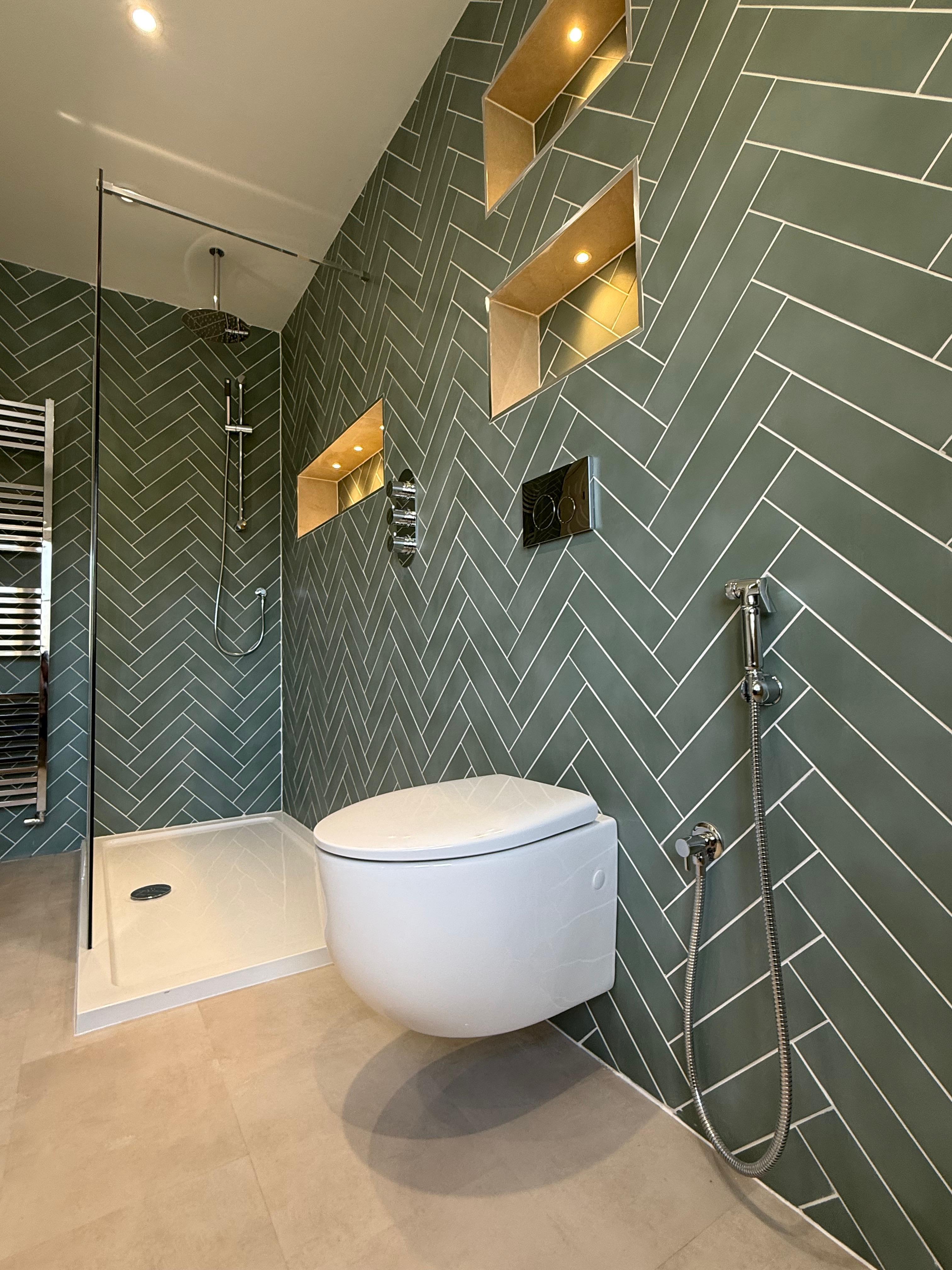 Green herringbone wall tiles with a wall-hung toilet and lit brass niches
