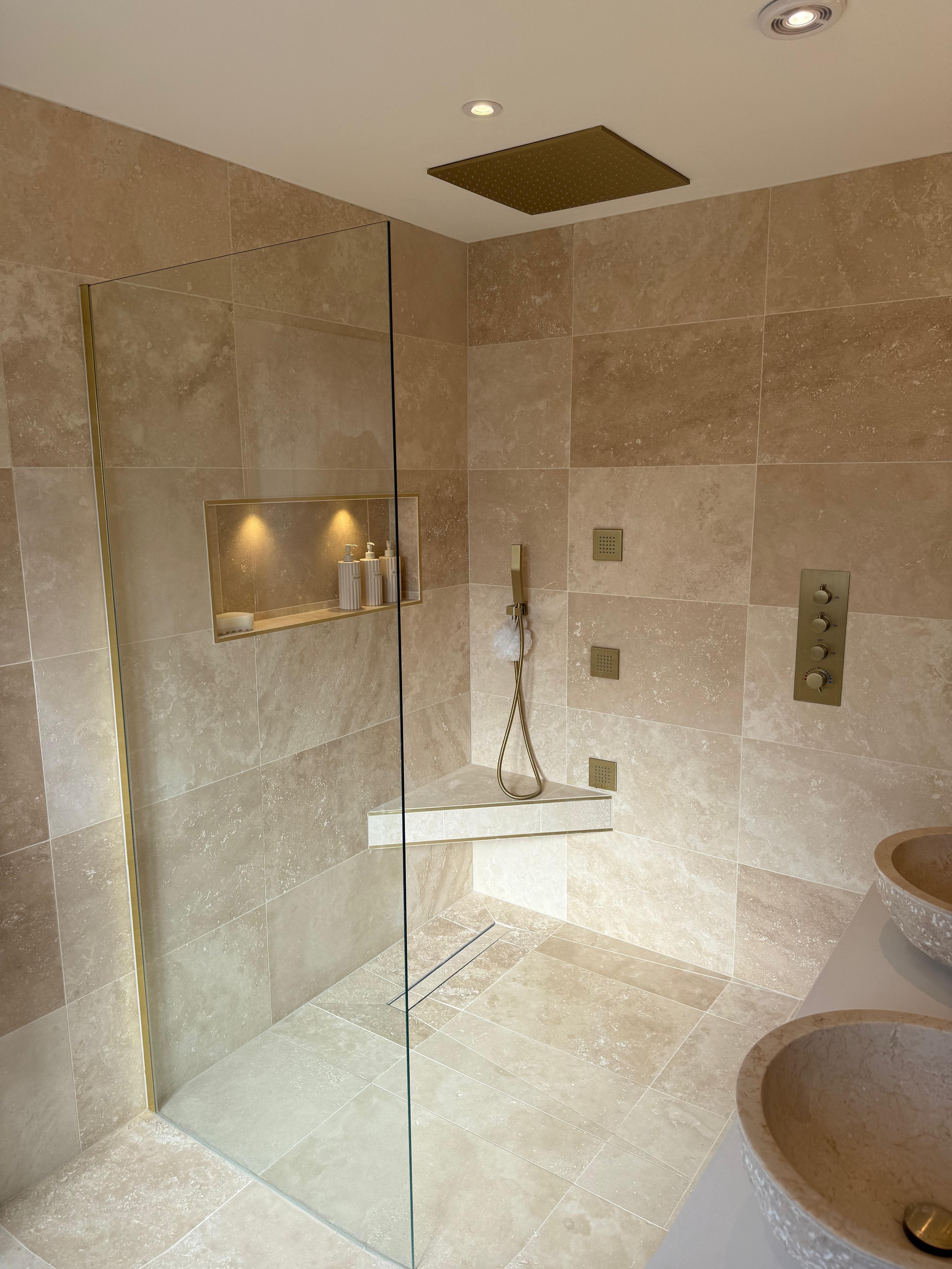 Walk-in shower with a frameless glass screen, brass ceiling shower and a lit niche